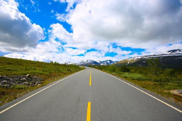 An open road stretching through a green valley toward distant mountains