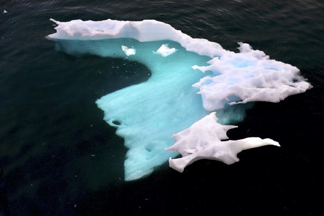 Iceberg with small tip above water and large glowing mass visible below the surface